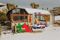 a small house with a woman sitting on a bench in the snow